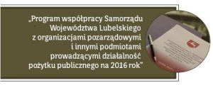 Biały napis na oliwkowym tle: Program współpracy Samorządu Województwa Lubelskiego z organizacjami pozarządowymi i innymi podmiotami prowadzącymi działalność pożytku publicznego na 2016 rok. Obok zdjęcie przedstawiające akt z logiem Województwa Lubelskiego i leżący na nim długopis.