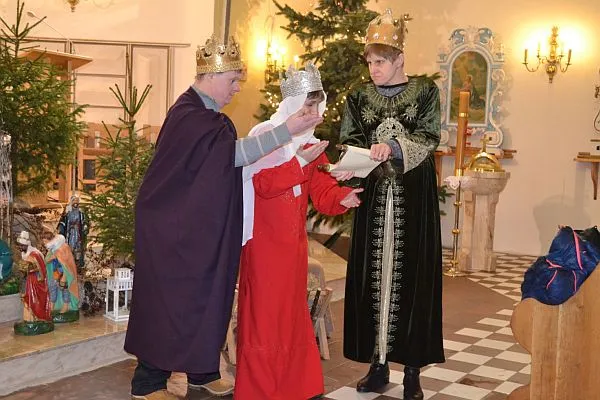 Dwóch mężczyzn i kobieta stoją na środku. Mężczyzna po prawej trzyma otwarty pergamin. Mężczyzna po lewej trzyma wyciągniętą rękę przed siebie. W środku stoi kobieta.
