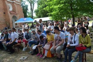 Ludzie siedzą na ławkach wśród drzew. Są to kobiety i mężczyźni.