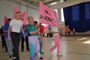 Na sali jest grupa osób. Osoby trzymają wysoko plakat z napisem WTZ Janowski.