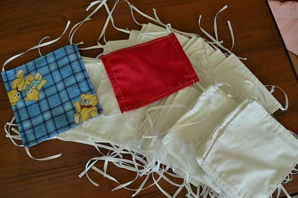 Na stole leżą maseczki. Większośc jest biała, ale jest także czerowna i niebieska w kratkę z misiem.