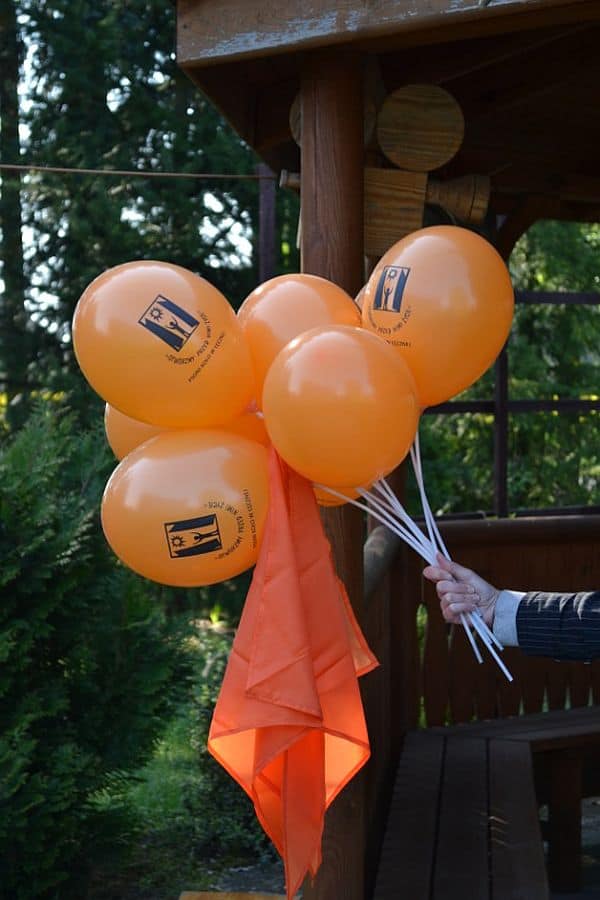 Kilka pomarańczowych balonów, które są w czyjejś ręce. Z balonów wystaje pomarańczowa chusta.