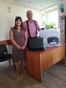 Kobieta i mężczyzna stoją przy biurku. Na nim stoi laptop oraz drukarka w pudełku.