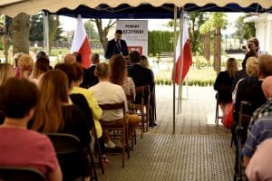 Uczestnicy zwróceni tyłem do obiektywu siedzą na krzesłach.