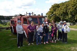 Grupa osób pozuje do zdjęcia. Za nimi stoi samochód straży pożarnej.