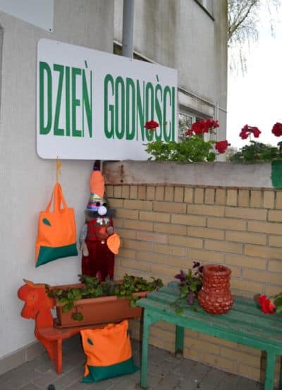 Plakat z napisem “Dzień Godności”. Balkon udekorowany jest różnorodnymi roślinami, które stoją na ławce.