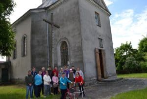 Wycieczkowicze w tym dwie osoby poruszające się przy pomocy balkoników pozują na tle szarego budynku kościoła.