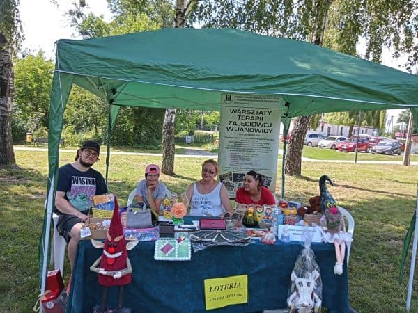 Namiot wystawowy Warsztatów Terapii Zajęciowej w Janowicy obsługiwany przez trzy kobiety i mężczyznę, eksponują liczne rękodzieła.