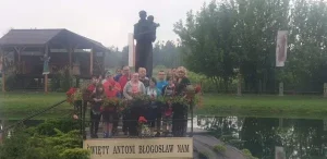 Grupa osób stoi przed figurą św. Antoniego na środku jeziorka. Wszyscy pozują do zdjęcia.
