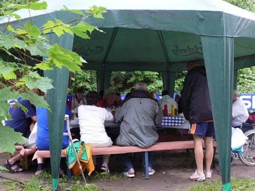 Na zdjęciu pod dachem zielonego namiotu uczestnicy stołują się grillem.