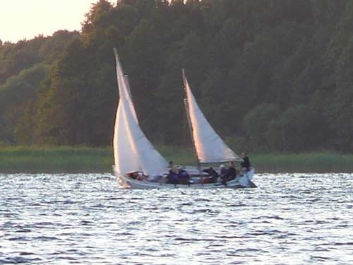 Na zdjęciu płynąca żaglówka z pełnymi żaglami w promieniach zachodzącego lub wschodzącego słońca