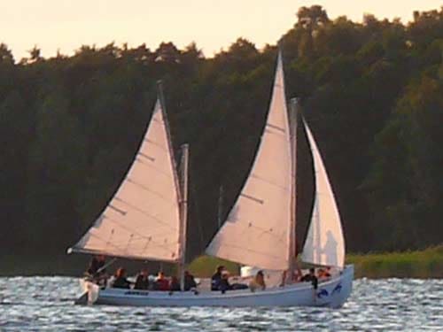 Na zdjęciu płynąca żaglówka z pełnymi żaglami w promieniach zachodzącego lub wschodzącego słońca