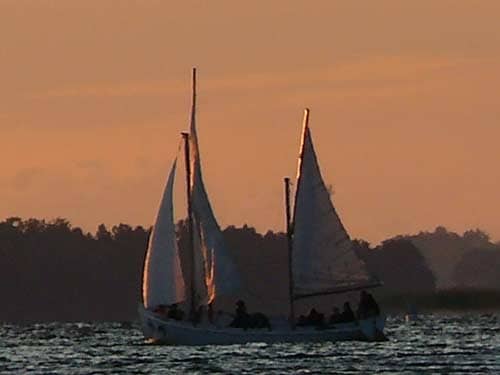 Na zdjęciu płynąca żaglówka z pełnymi żaglami w promieniach zachodzącego lub wschodzącego słońca