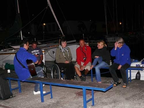 Na zdjęciu grupa osób wspólnie śpiewa przy akompaniamencie gitary, na której gra mężczyzna siedzący tyłem do fotografa. Wśród uczestników jest kobieta na wózku.