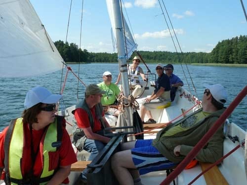 Na zdjęciu grupa uczestników w kamizelkach siedzi w żaglówce.