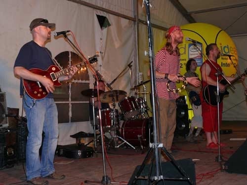 Na zdjęciu muzycy dajakoncert na scenie grając na gitarach elektrycznych i tamburynie.