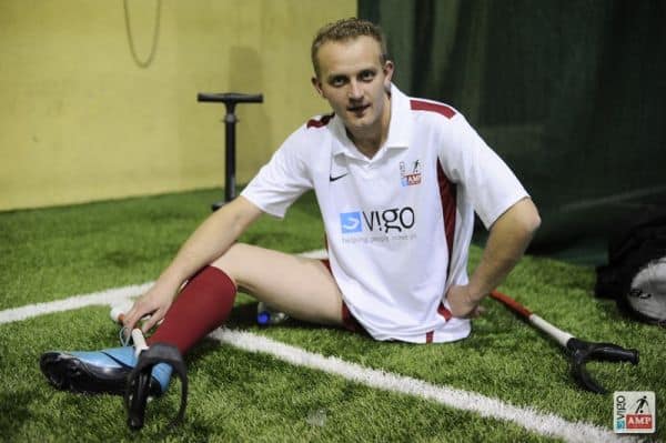 Na zdjęciu odpoczywa w treningu jeden z piłkarzy siedząc na murawie.