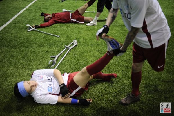 Na zdjęciu piłkarze wzajemnie rozgrzerwają sobie mięsnie nóg rozciągając je.