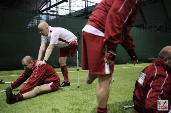 Na zdjęciu piłkarze pomagają sonbie w rozciąganiu. Siedzący robi sklón do przodu, a drugi pcha jego plecy by skłon był niższy.