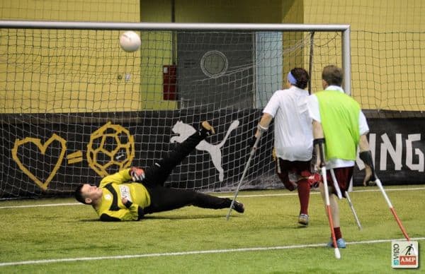 Na zdjęciu bramkarz rzuca się na piłkę wykopaną przez piłkarza.