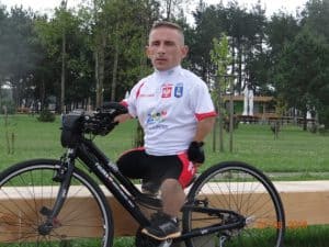 Na zdjęciu pozuje na swoim rowerze Andrzej Łukasik w sportowej białej koszulce, czarnych spodenkach i addidasach.