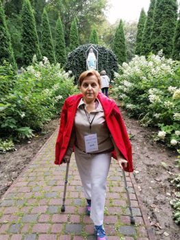 Na zdjęciu Krystyna o kulach spokojnie idzie spacerkiem w parku. W tle figura Matki Boskiej