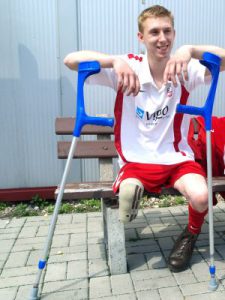 Na zdjęciu uśmiecha się Kamil Misztal. Siedzi na ławce w stroju reprezentacji Polski, opiera ręce o niebieskie kule.