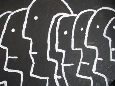 Obraz pod tytułem "Ludzkość". Białe kontury profili twarzy ludzi gęsto obok siebie na czarnym tle.