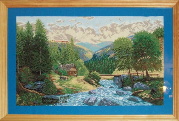 Haftowany obraz autorstwa Moniki  przedstawiająct krajobraz górski. Od dołu obrazu ku jego centrum płynie rzeka, skaliste nbiskie brzegi. Na jednym z nich wśród drzew lasu stoi domek drewniany. W tle lasy i ośnieżone szczyty pasma gór.