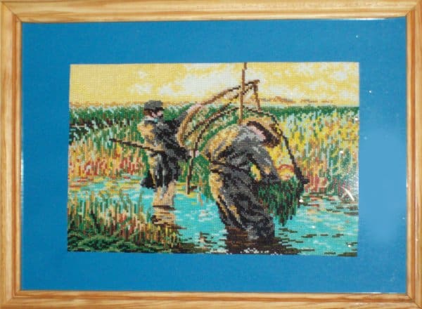 Haftowany obraz Moniki przedstawiający dwóch mężczyzn podczas żniw, zbiorów zboża na podmokłym polu. 