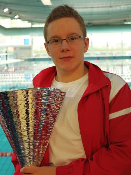 MAteusz Bartnik pozuje z pucharem w dłoniach na tle basenu