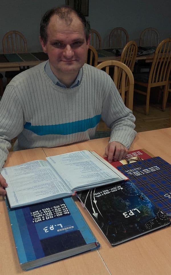 Krzysztof Dalentka siedzi przy stole nad swoimi ręcznie zapisanymi dziennikami notowań listy przebojów Trójki