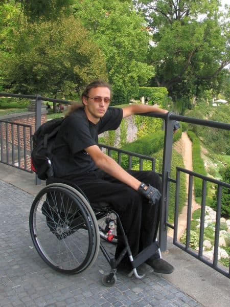 Artur Jurek na wózku pozuje do sjęcia stojąc na mostku w parku i trzymając się poręczy.