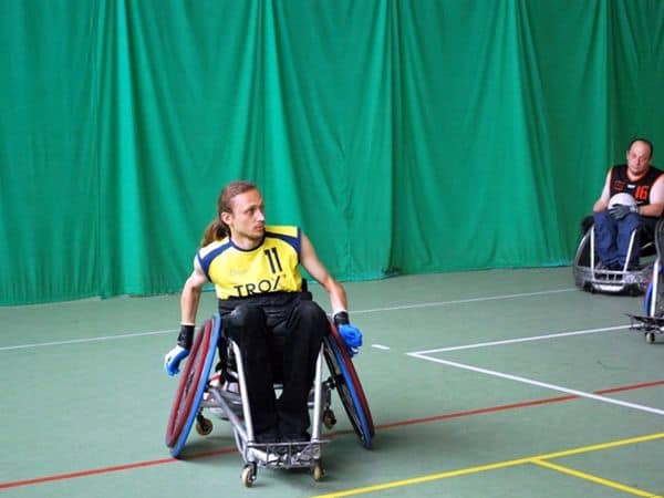 Artur Jurek na specjalnym wózku do gry w koszówkę w hali sportowej.