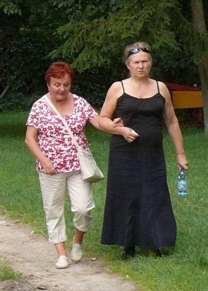 Kobieta prowadzi pod rękę starszą emerytkę.