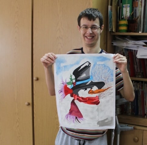 Kamil prezentuje do zdjęcia ryseunek bałwana z szalikiem , nosem z marchewki i w czarnym cylindrze.