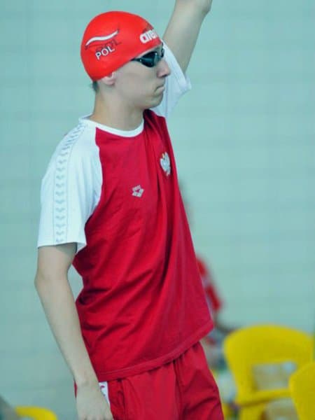 Artur Pióro mach w kieeunku trybun stojąc w czepku i z okularami pływackimi.