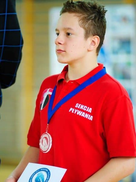 Mateusz Bartnik z medalem na szyi i w czerwonej koszulce szkolnej sekcji pływackiej