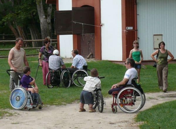 Ludzie w mniejszych grupkach nawóżkach na gruntowej drodze pod stajniami.