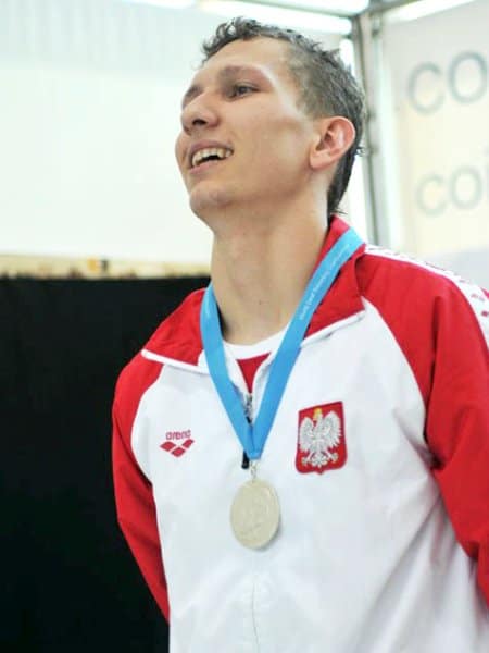 Artur Pióro z medalem na piersi stoi i jest szczęśliwy,