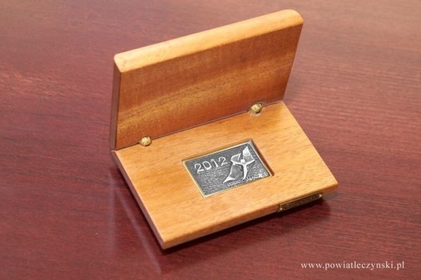 Nagroda w postaci drewnianej szkatułki z metalową żłobioną tabliczką w środku.