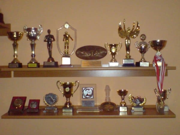 Dwie półki pełne pucharów zdobytych na zawodach pływackich.