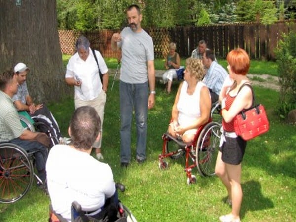 Grupa słucha przewodnika wycieczki stojąc w kręgu wokół niego.