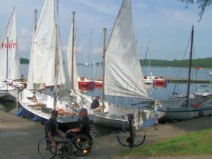 Dwaj mężczyźni na wózkach na przystani przed żaglówkami,