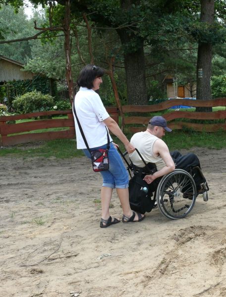 Kobieta pomaga wózkowiczowi przejechać piach
