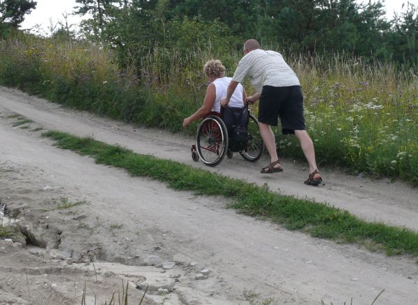Mężczyzna pcha wózek z kobietą po nieutwardzonym szlaku.
