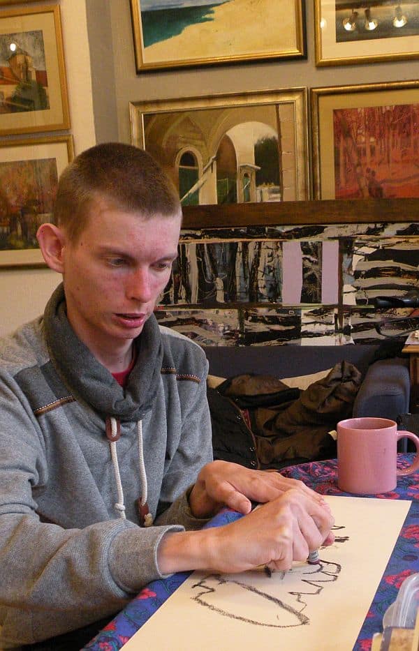 Damian Czerwiński podczas malowania pastelami olejnymi przy stole.