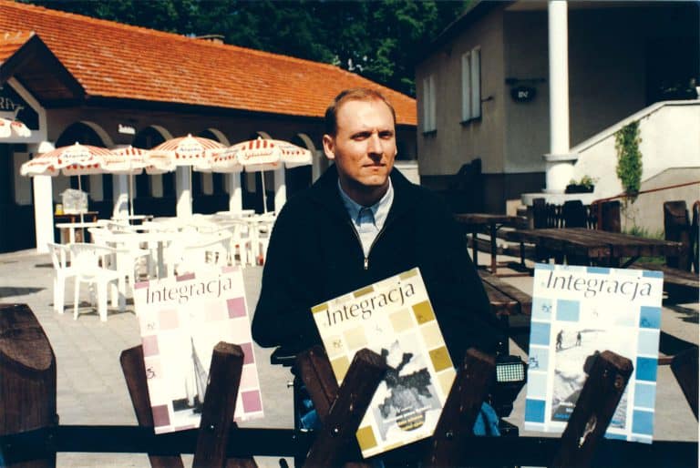 Na zdjęciu Piotr Pawłowski. W tle restauracja z ogródkiem. Na dole zdjęcia wklejone trzy numery magazynu Integracja
