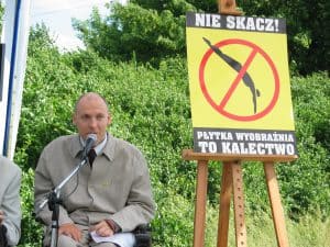 Piotr Pawłowski przemawia obok plakatu: Nie skacz! Płytka wyobraźnia to kalectwo
