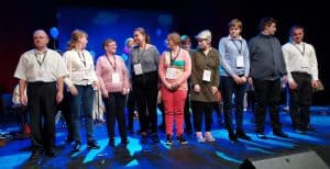 Na zdjęciu zespół „Bębnoludy” stojący na scenie, w tle niebieskie światło.